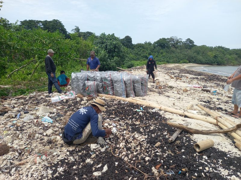 Warga sekitar sedang membersihkan batu bara yang sebelumnya di muat oleh tongkang BG Titan 14 yang kemudian tumpah ke perairan laut di wilayah labuan.